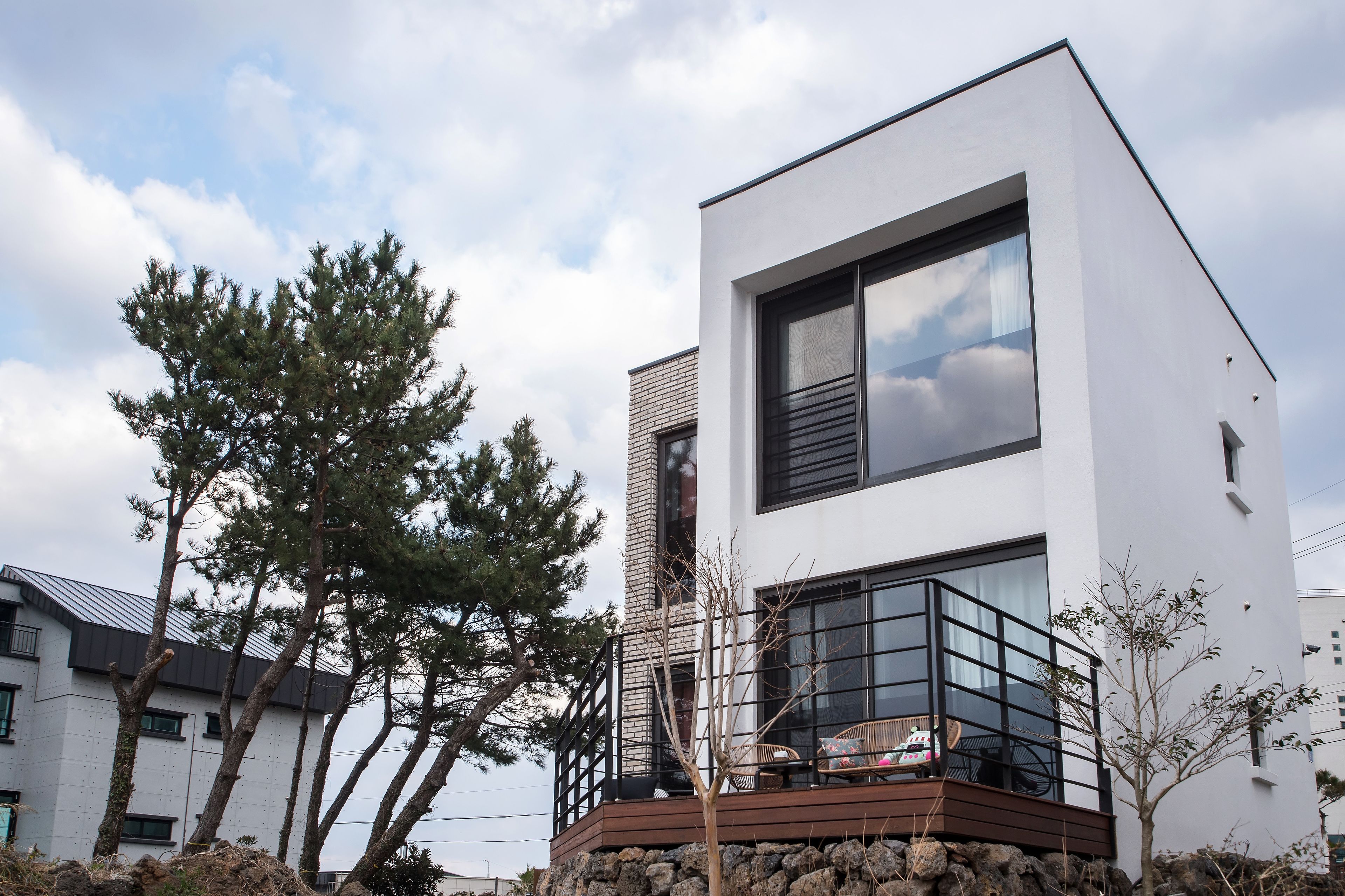 A modern two-story building with a white facade, large windows, and a balcony with outdoor seating.