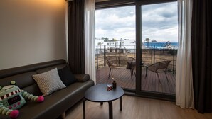 Un salon moderne avec un canapé, une petite table et une vue sur une terrasse aménagée avec du mobilier d’extérieur.