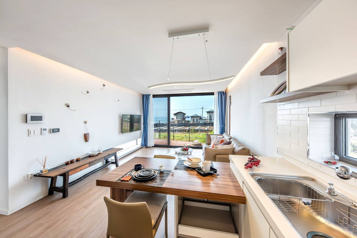 A modern kitchen with a wooden dining table, built-in appliances, and a large window offering a view of the outdoors.