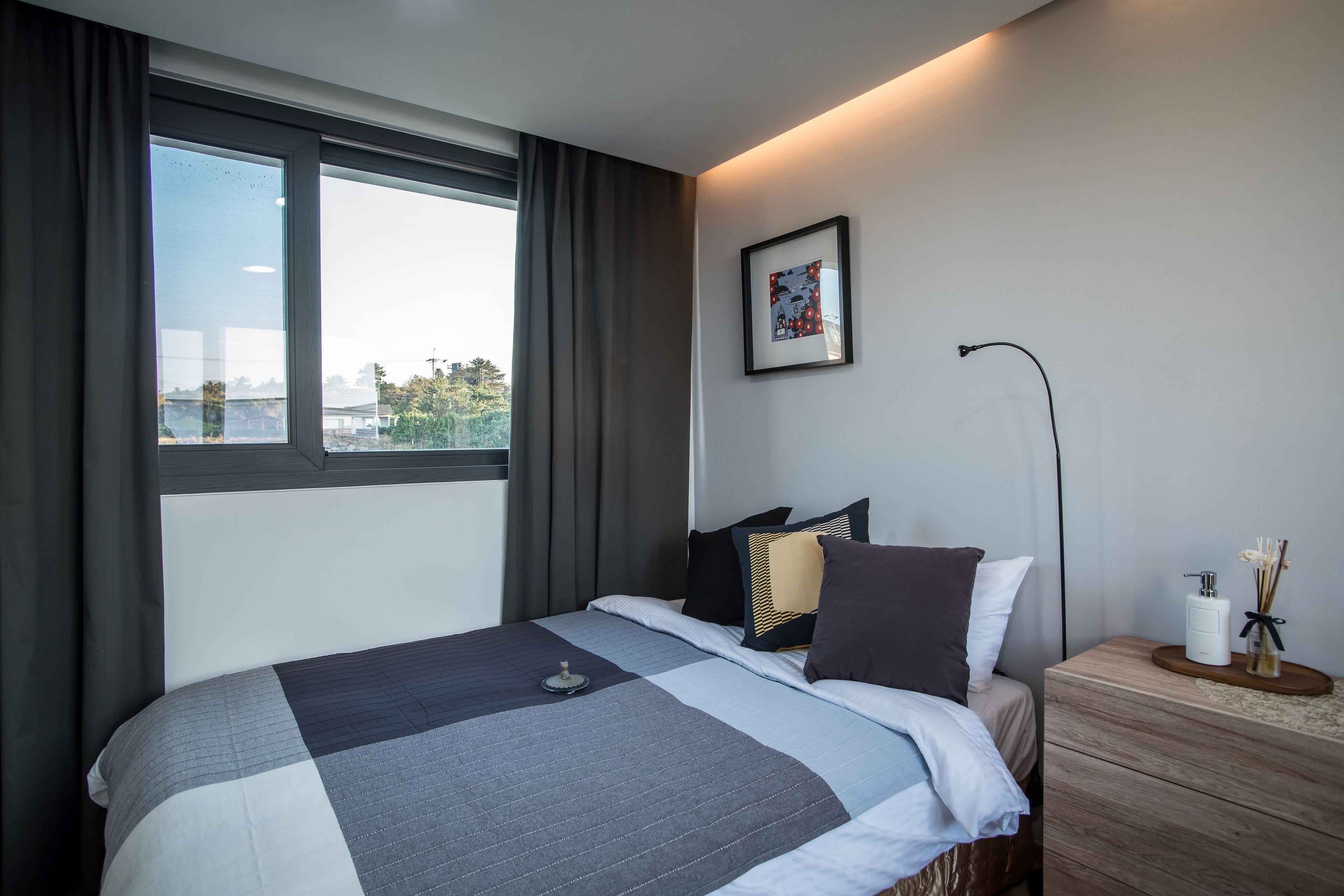 Una habitación de hotel moderna con una cama grande, una mesita de noche, una lámpara de escritorio y una ventana con cortinas.