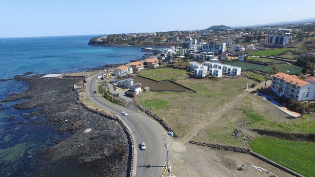 Une vue aérienne d’une ville côtière, avec une route qui serpente le long du littoral, des bâtiments et un pont reliant la ville au continent.