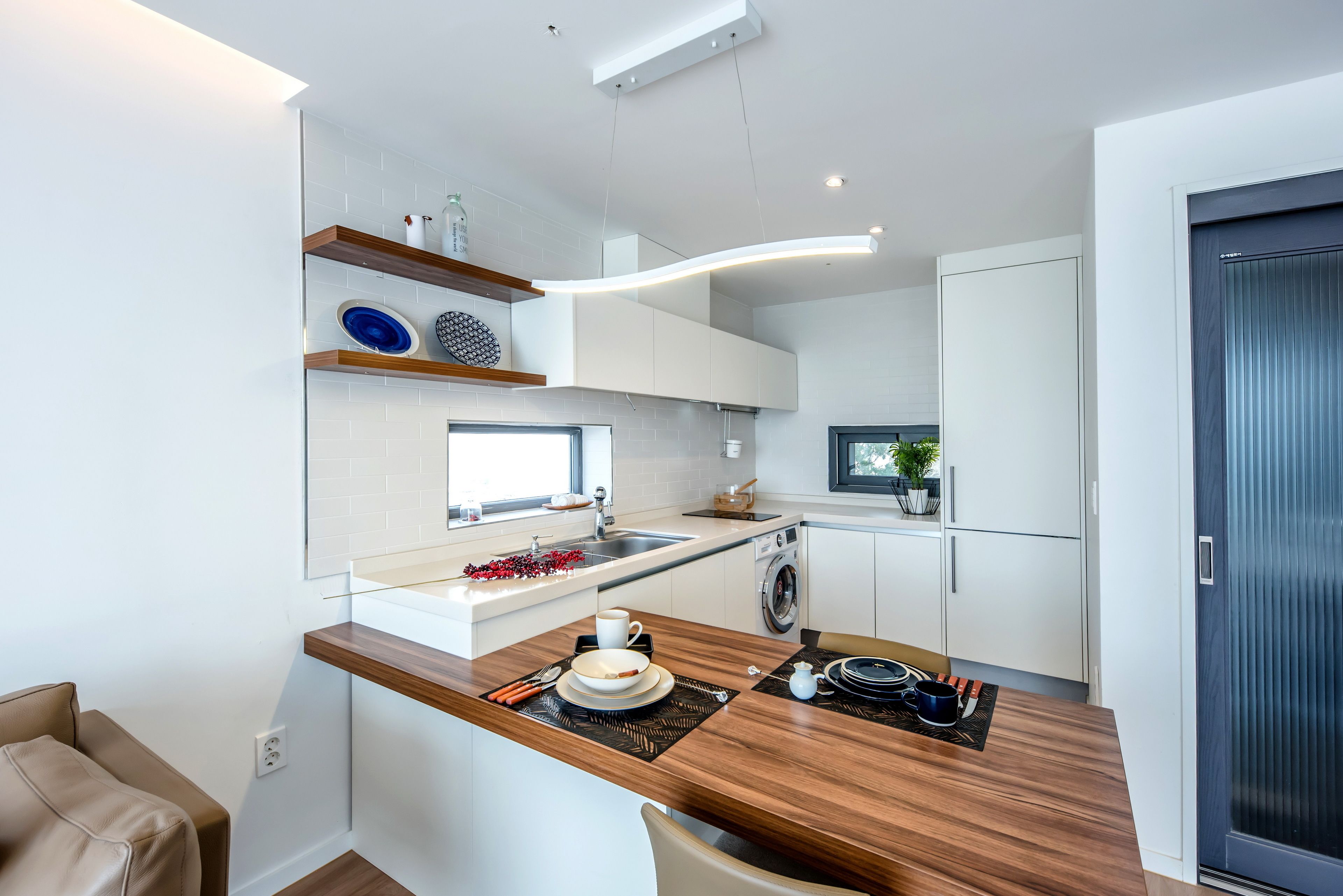 A modern kitchen with white cabinetry, a wooden countertop, and a built-in washing machine.