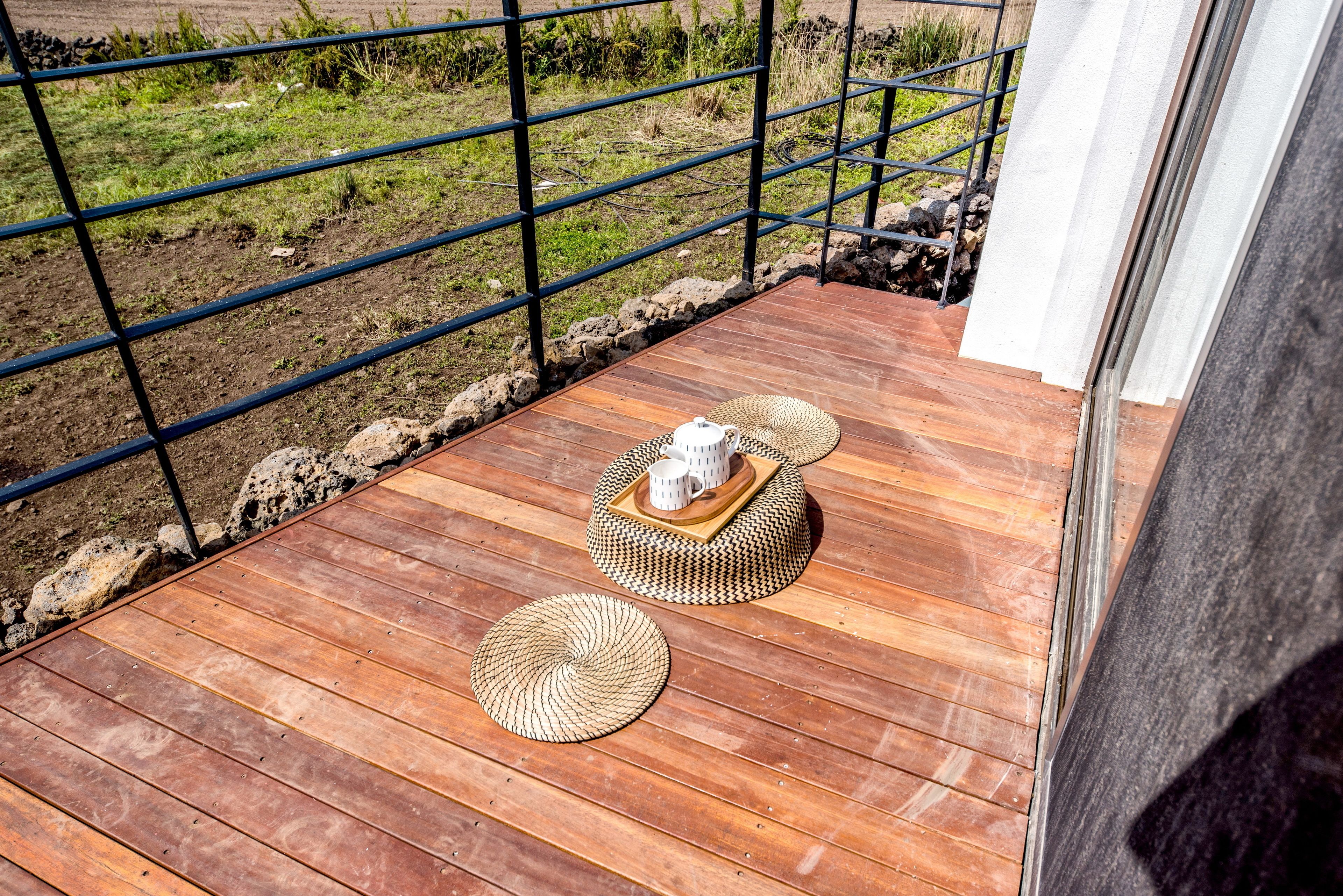 A wooden deck with a metal railing, two woven mats, and a small table with a cup and saucer.