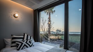 Une chambre avec une grande fenêtre, un lit avec une literie blanche et une vue sur une plage et des palmiers.