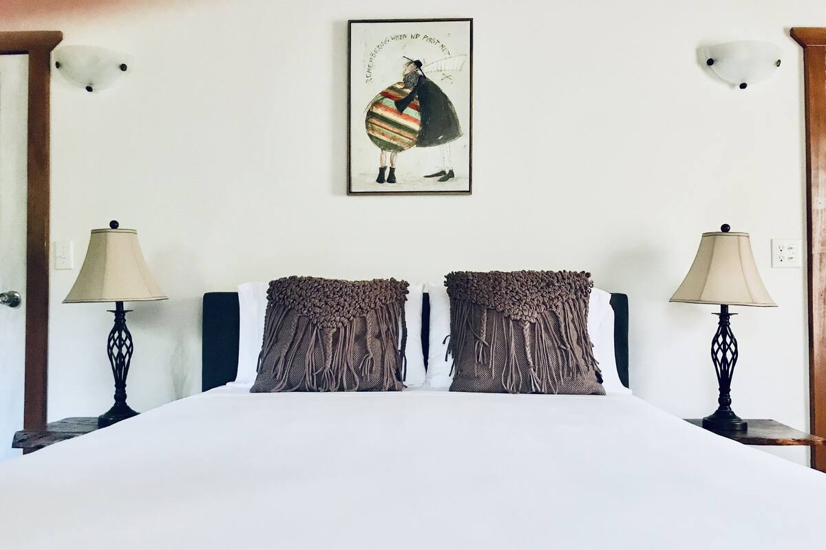Ein Schlafzimmer mit einem großen Bett, zwei Nachttischen, zwei Lampen und einem gerahmten Bild an der Wand.