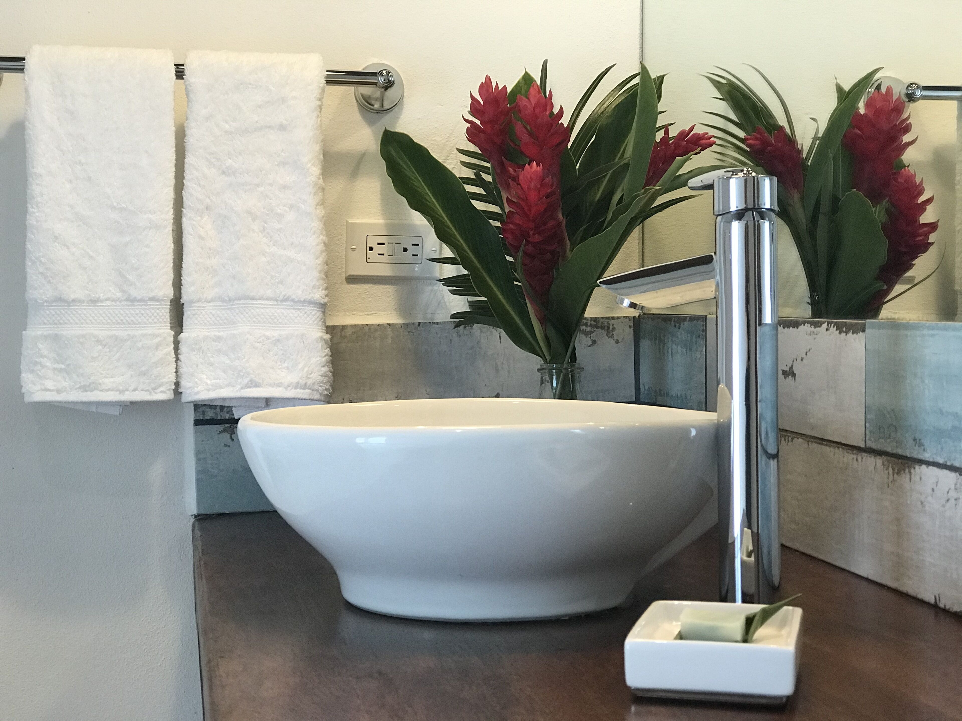 A bathroom with a white sink, a towel rack with white towels, and a vase with red flowers.