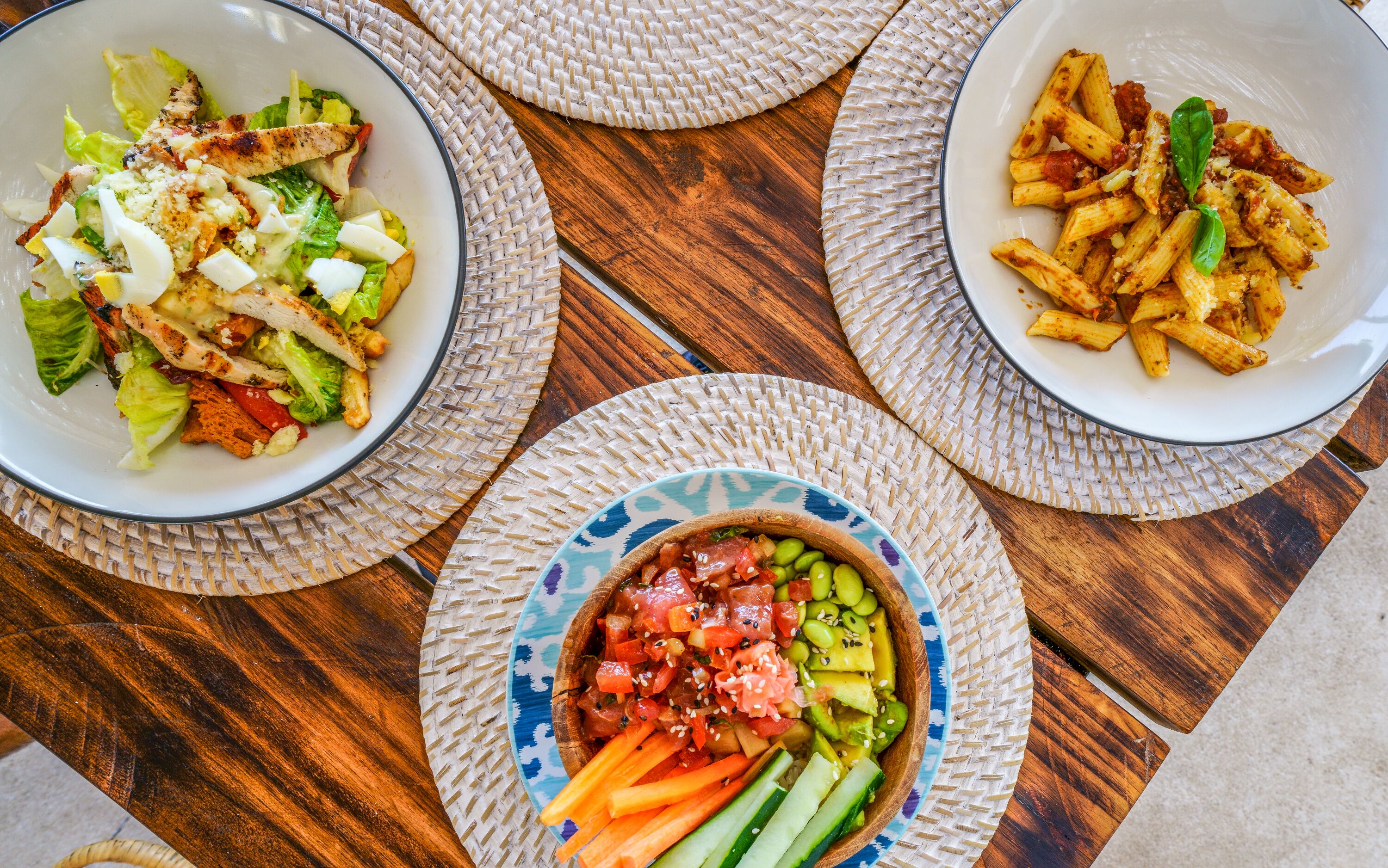 Three bowls of food on a wooden table with woven placemats.