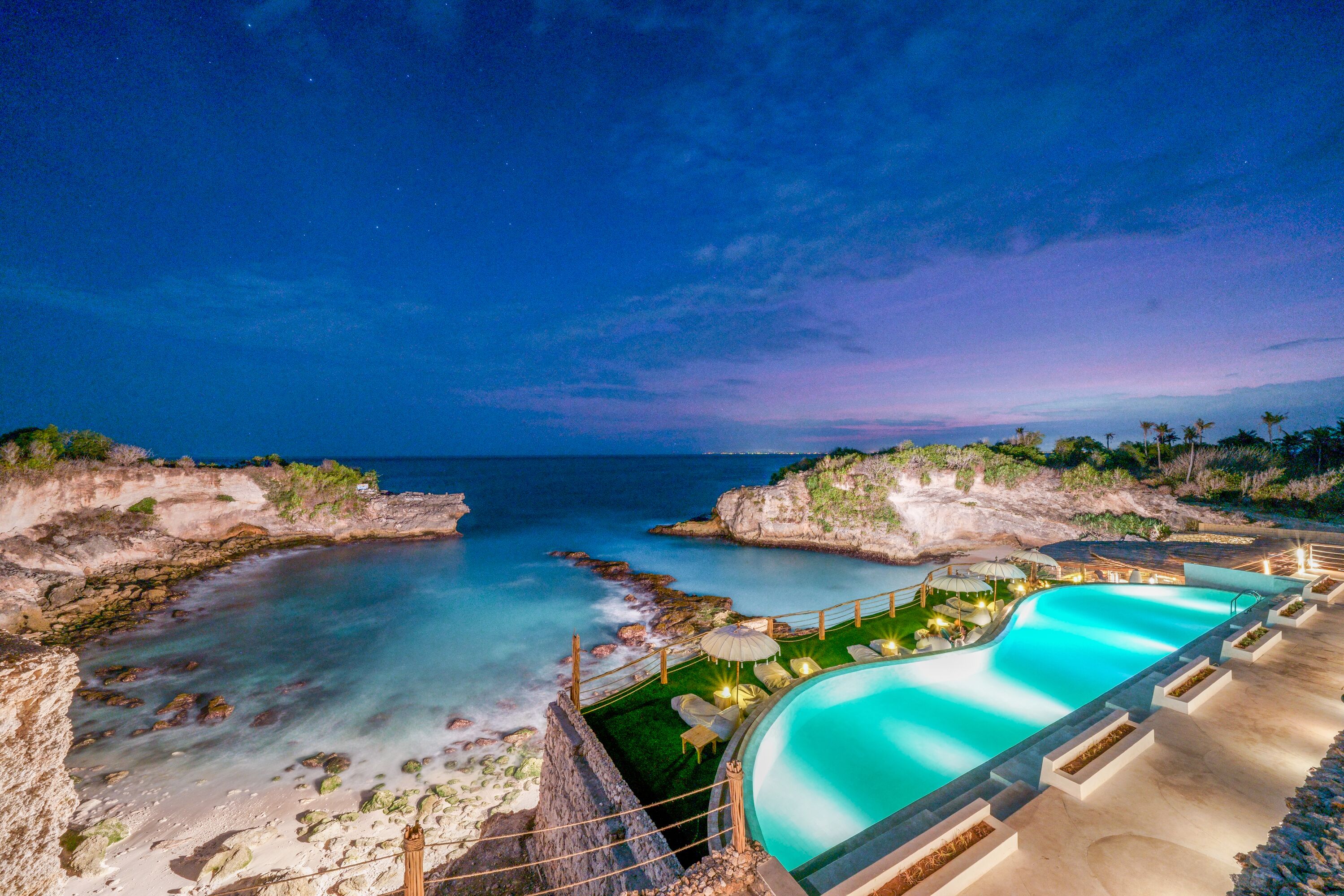 Piscina de un complejo turístico con vista al océano y a la costa rocosa.