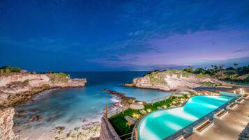 Piscina de un complejo turístico con vista al océano y a la costa rocosa.