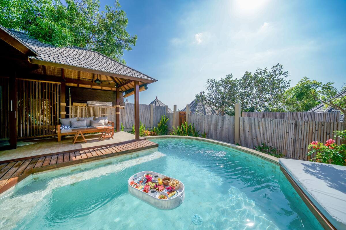 Ein Swimmingpool mit einer schwimmenden Bar, einer Holzterrasse und einem überdachten Sitzbereich.