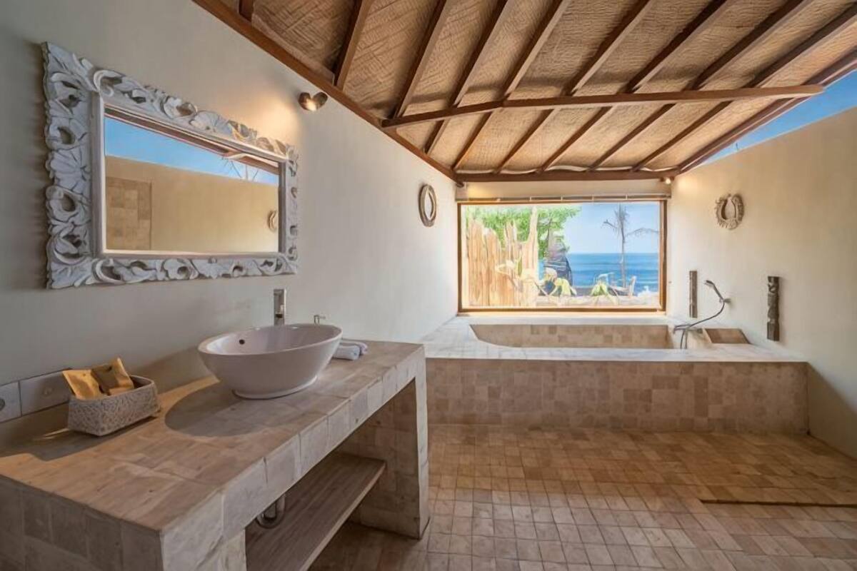 Ein Badezimmer mit großem Spiegel, einem Waschbecken, einer Badewanne und Blick auf den Strand.