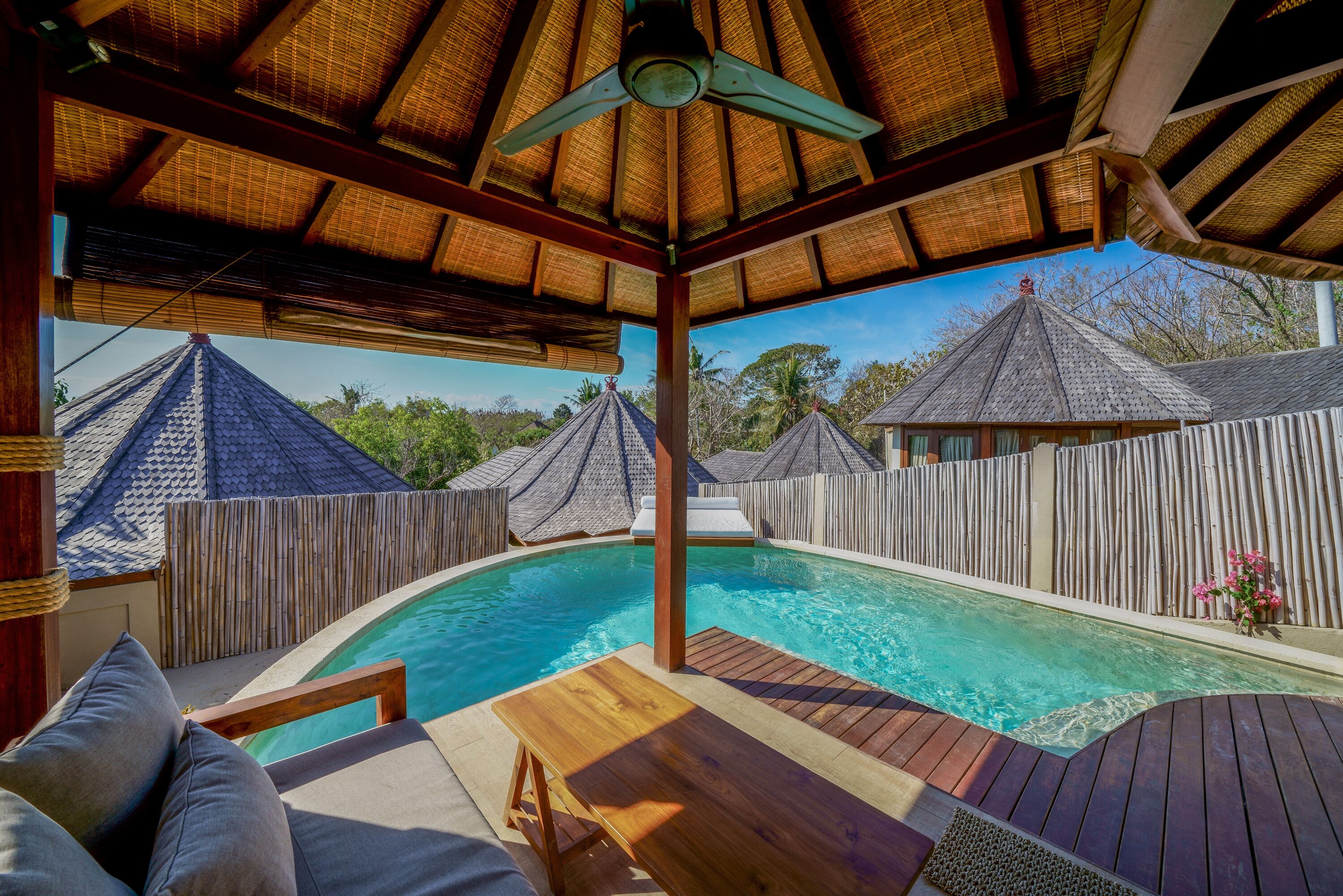 A pool area with wooden deck, lounge chairs, and a ceiling fan.