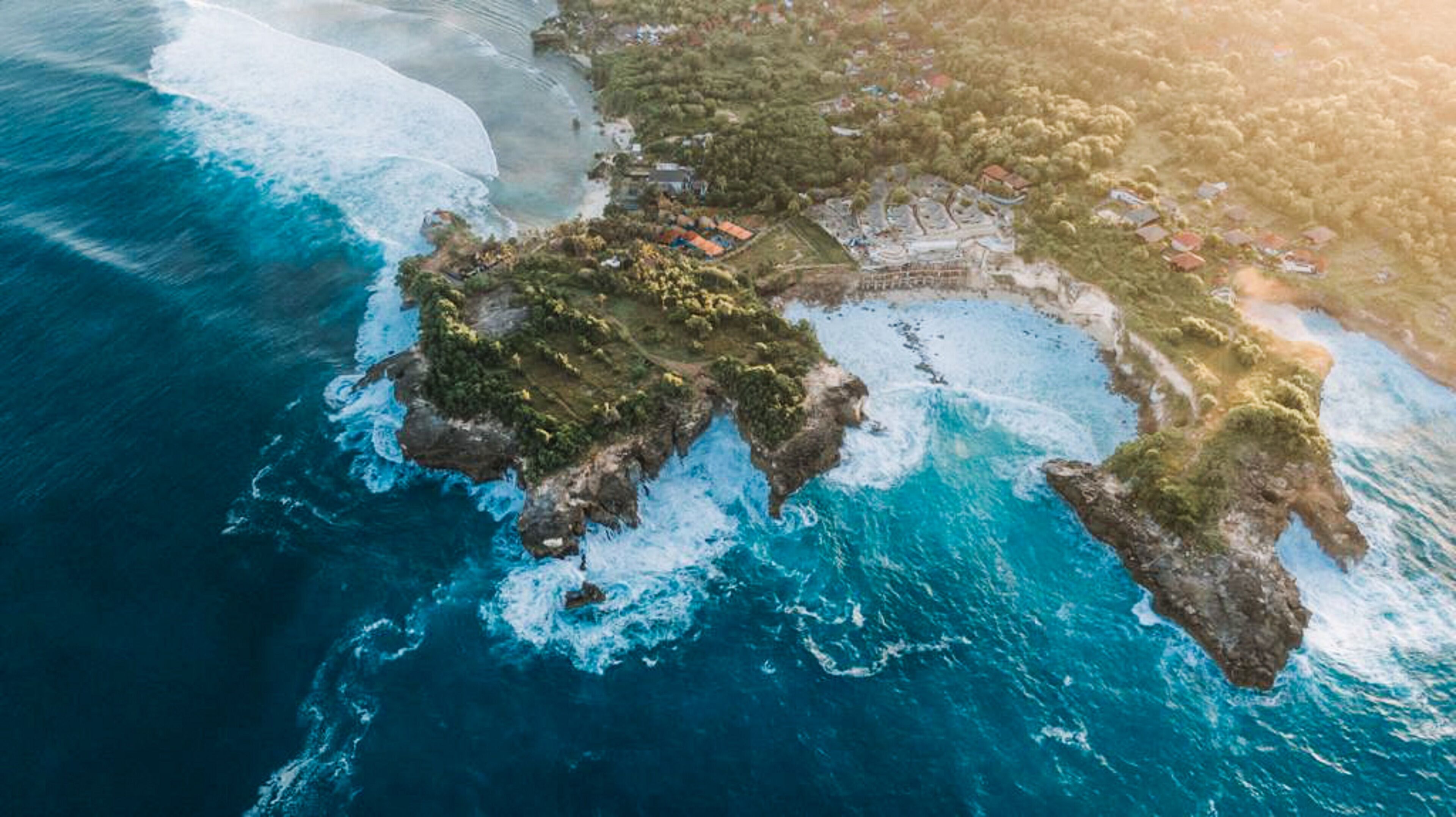 An aerial view of a coastal area with rocky terrain, clear blue waters, and scattered buildings.