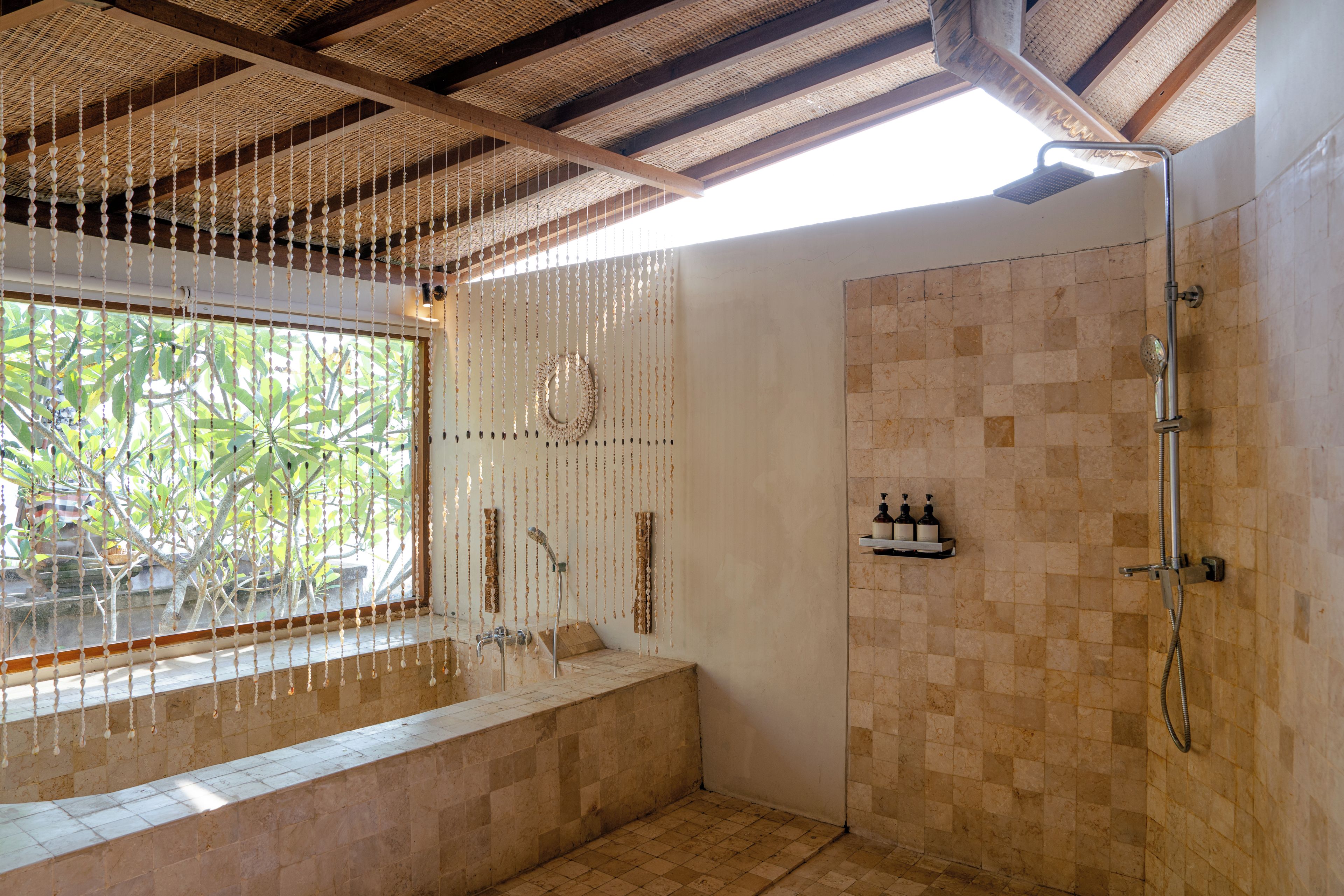 A bathroom with a shower, a bench, and a window with a view of greenery.