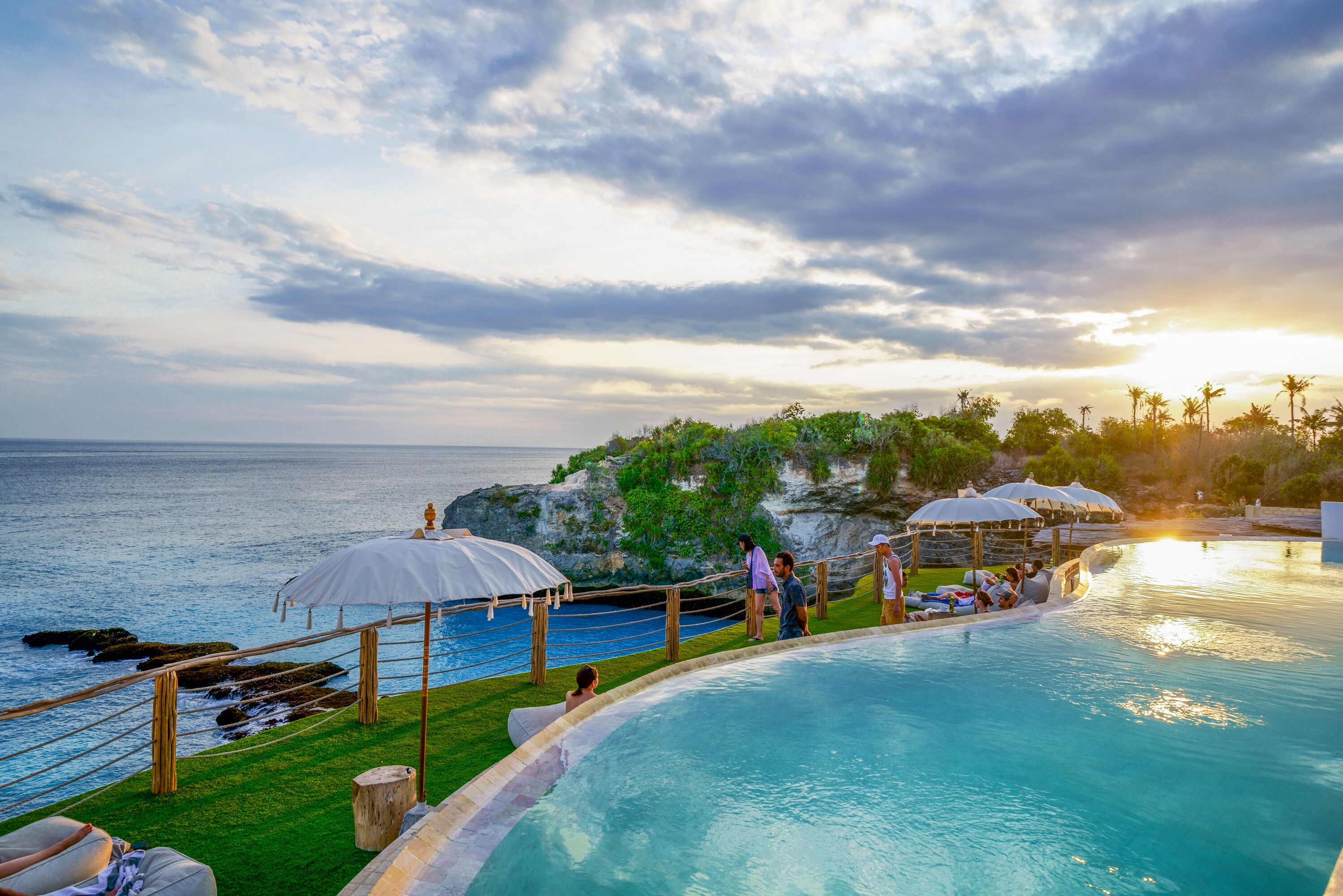 A poolside area with a view of the ocean, wooden deck, and umbrellas.