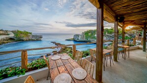 Un espace extérieur aménagé pour prendre les repas, offrant une vue sur la mer et la côte rocheuse.