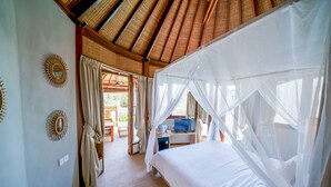 Une chambre avec un lit recouvert d’une moustiquaire, un bureau avec une chaise et une vue sur l’extérieur.