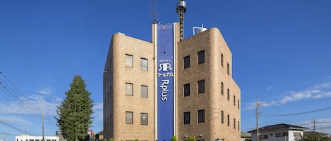 A hotel with a prominent blue vertical sign, a brick facade, and a tall antenna on the roof.