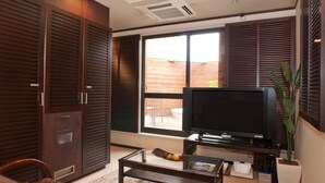 A living room with a flat-screen TV, wooden shutters, a glass coffee table, and a potted plant. - Hotel Rplus - Adults only (Yachiyo)