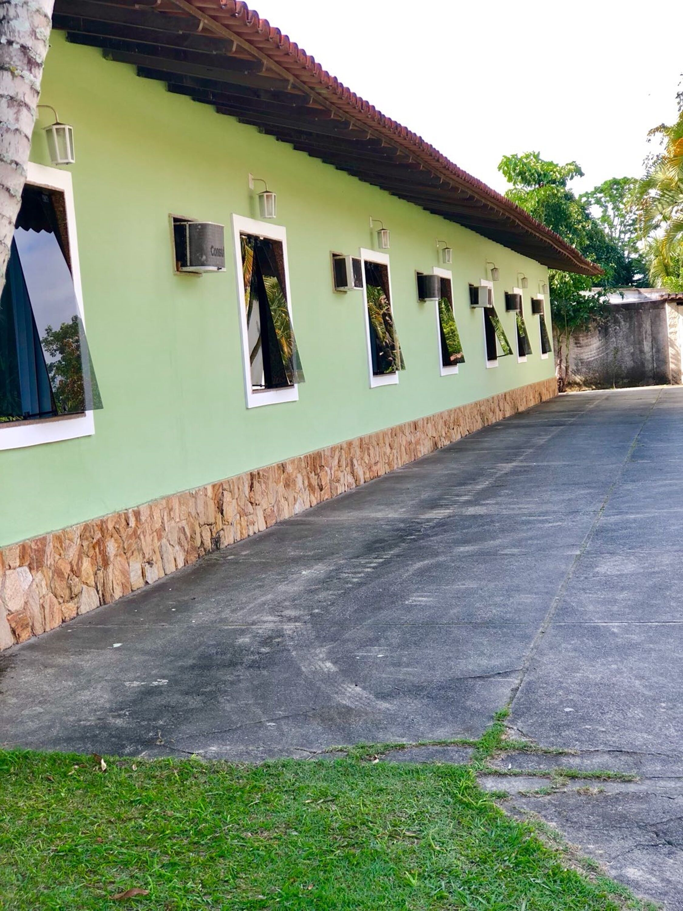 Um edifício com fachada verde, base de pedra e telhado de telhas. Várias janelas com plantas visíveis.