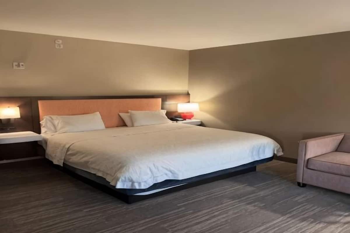 A hotel room with a bed, bedside lamps, a nightstand, and a chair.