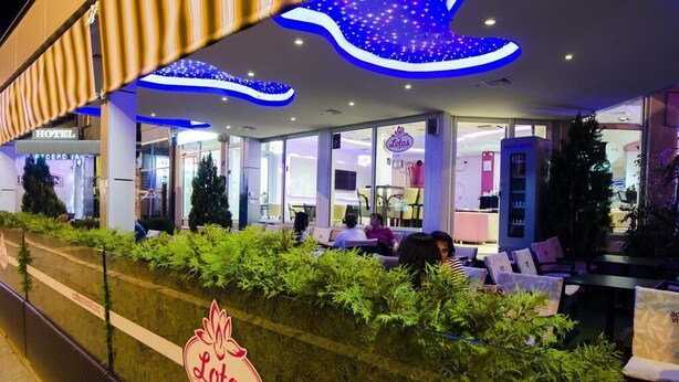 Une vue de l’extérieur d’un hôtel, avec un espace aménagé pour s’asseoir, une enseigne indiquant « Lotus » et une autre indiquant « Hôtel ».