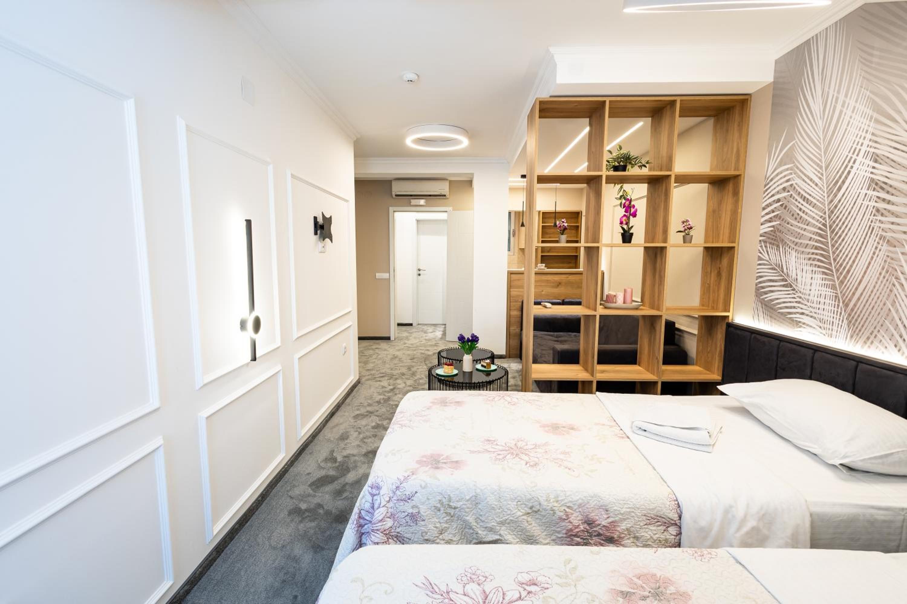 A hotel room with a bed, a wooden shelving unit, and a wall with a leaf pattern.