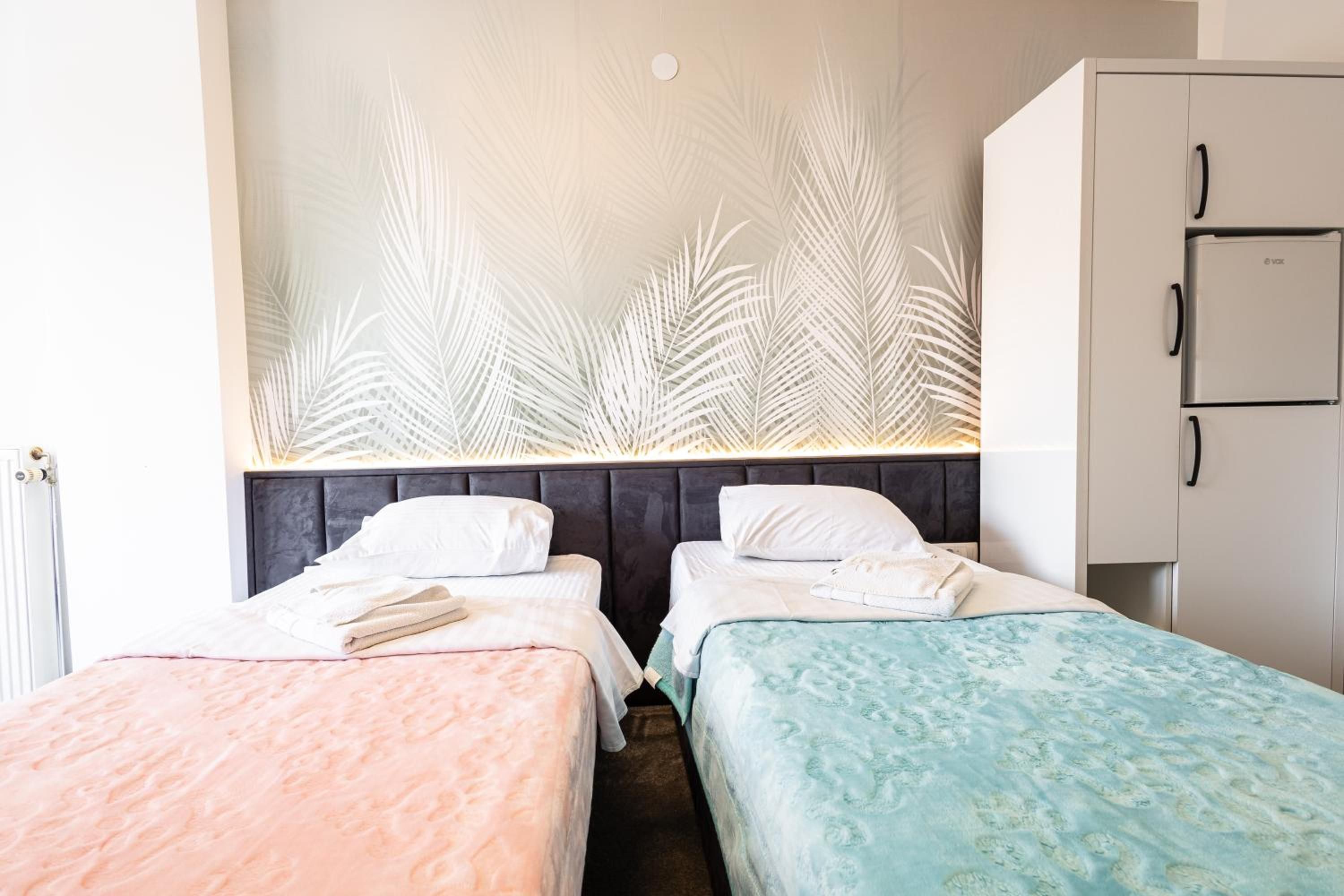 A hotel room with two beds, a wardrobe, and a wall with a leaf pattern.