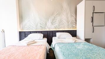 A hotel room with two beds, a wardrobe, and a wall with a leaf pattern.