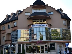 Un edificio con un letrero que dice "Poliklinika NISMEDIC" y un café llamado "Cafe Postojnicara" en la planta baja.