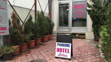 Entrada de un hotel con un letrero que dice 'RECEPCIA HOTEL' y un cartel de estacionamiento.