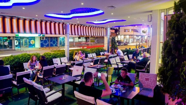 Un espace de restauration en plein air, avec des tables et des chaises, entouré de verdure et agrémenté d’un design moderne au niveau du plafond.