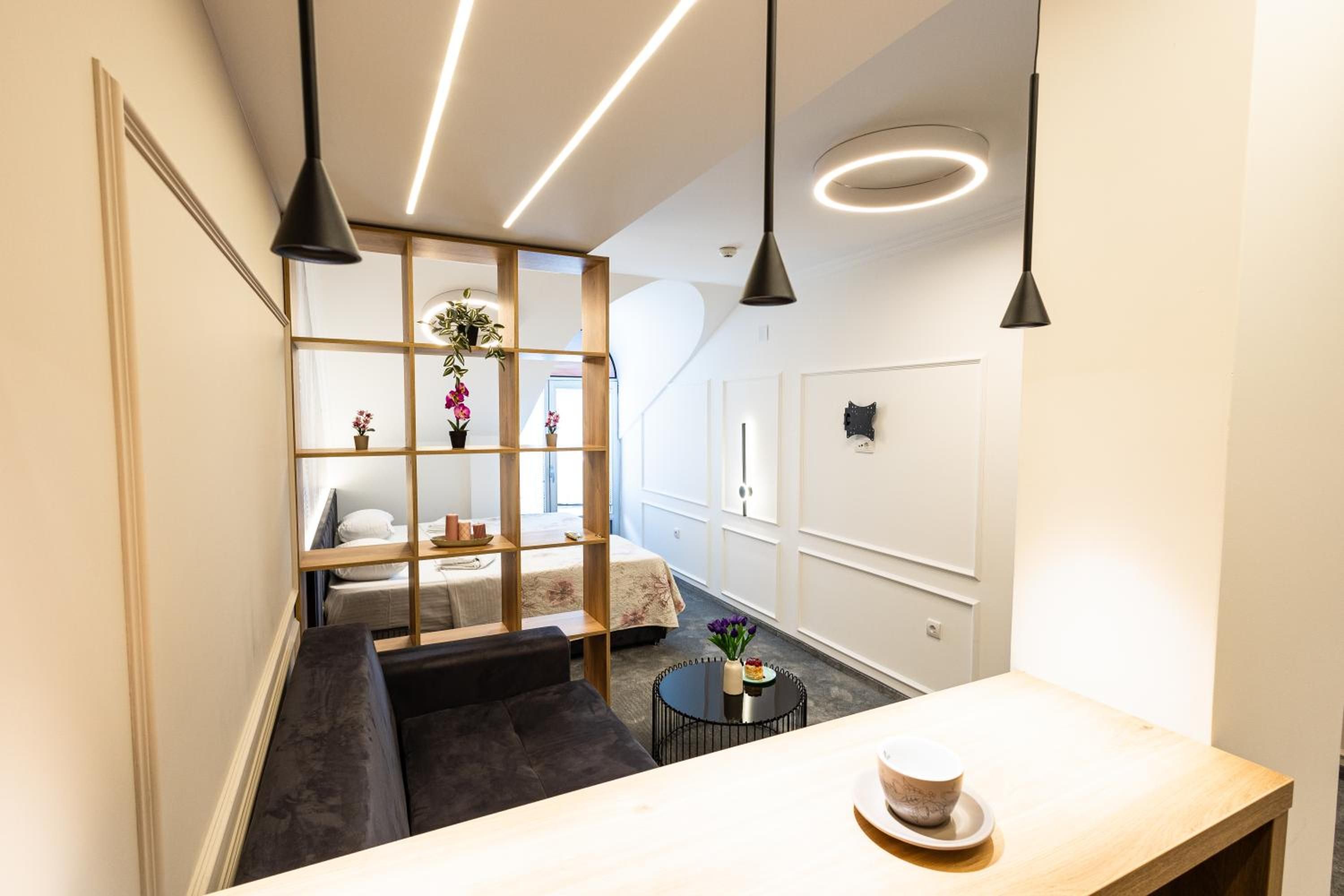 Habitación de hotel moderna con separador de madera, un sofá, una pequeña mesa redonda con una taza e iluminación colgante.
