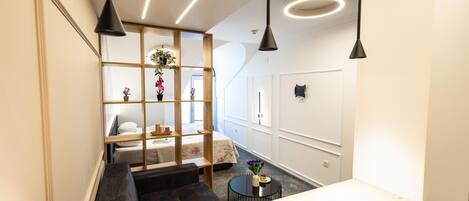 Habitación de hotel moderna con separador de madera, un sofá, una pequeña mesa redonda con una taza e iluminación colgante.