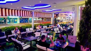 Un espace de restauration en plein air, avec des tables et des chaises, entouré de verdure et agrémenté d’un design moderne au niveau du plafond.
