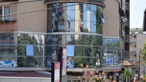 Un hôtel doté d’une façade moderne en verre, d’une enseigne bien visible indiquant « LOTOS », et d’un magasin « MANUEL » situé en dessous.