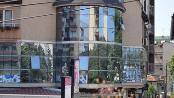 A multi-story hotel with a curved glass facade, balconies, and a visible ground floor with shops.