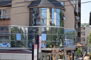 Un hotel de varios pisos con fachada de vidrio curvo, balcones y una planta baja visible con tiendas.
