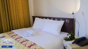 Une chambre d’hôtel avec un lit bien fait, un téléphone sur la table de chevet et un bouquet de fleurs sur la commode.