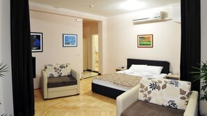 Une chambre d’hôtel comprenant un lit, deux fauteuils, un canapé, une table de chevet et un climatiseur fixé au mur.