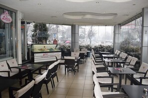 A restaurant with a gelato display, black and white chairs, and large windows. - Garni Hotel Lotos (Niš)