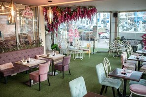 An indoor seating area with tables and chairs, a cushioned bench, and a hanging light fixture. - Garni Hotel Lotos (Niš)