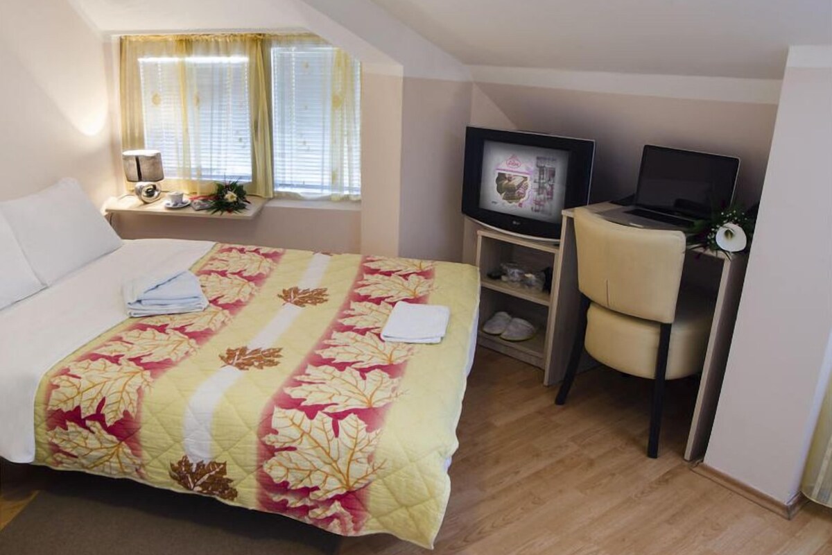 Une chambre d’hôtel avec un lit, un bureau avec un ordinateur, une télévision et une fenêtre avec des rideaux.