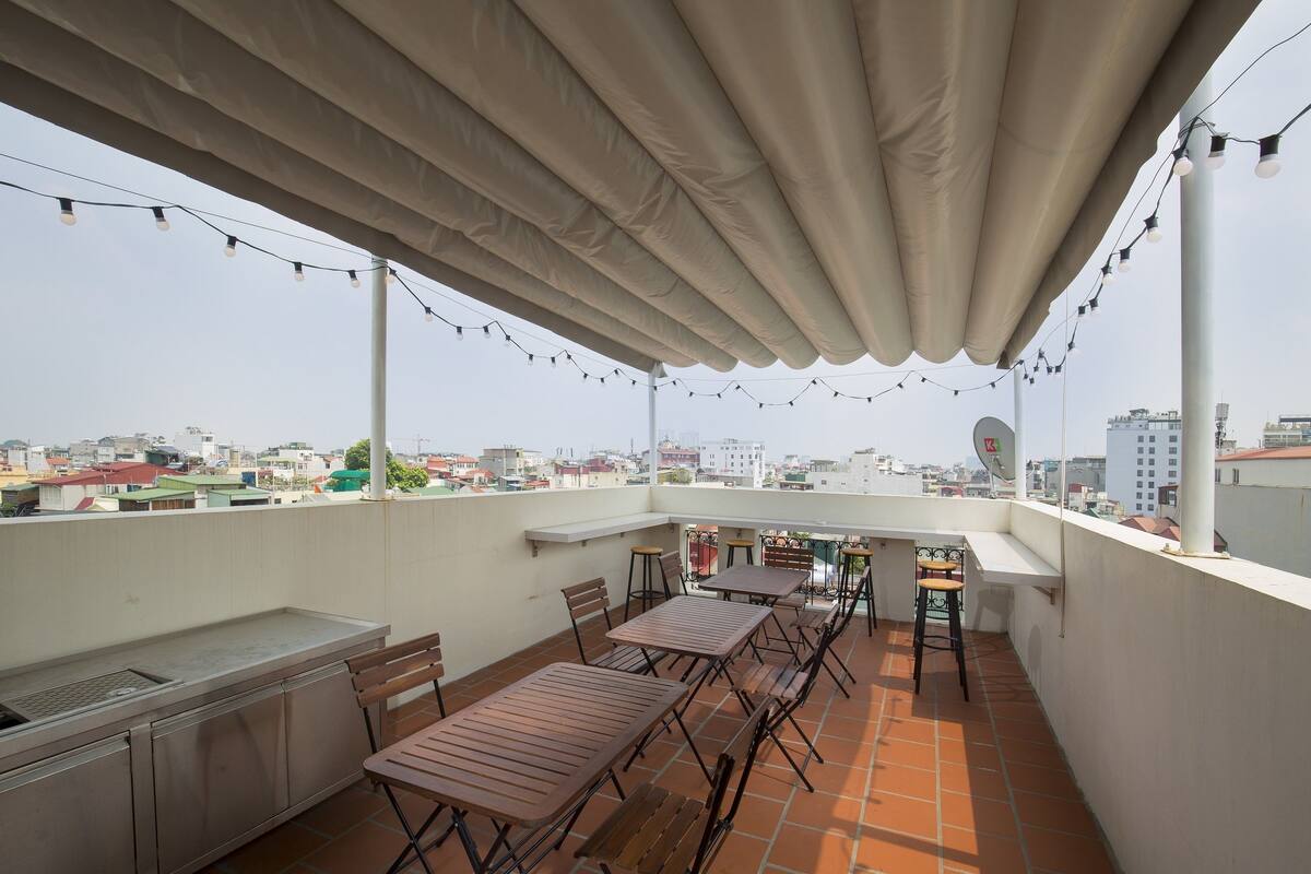 A rooftop terrace with a covered seating area, a sink, and a view of the cityscape.