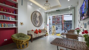 A modern interior with a sofa, green chair, wooden tables, and a large decorative wall piece. - D'annam Hostel Hanoi (Hanoi)
