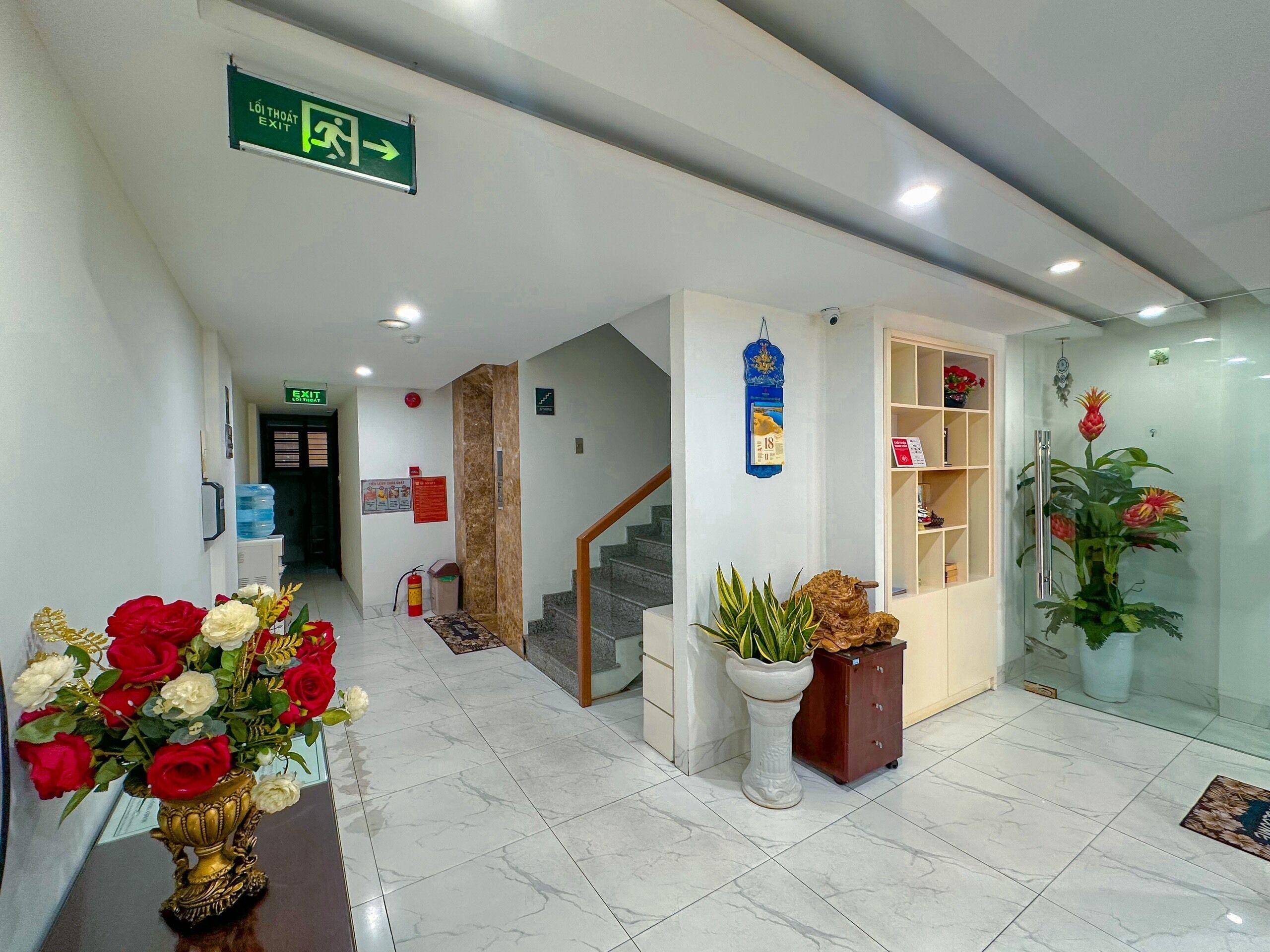 A hotel lobby with a reception desk, a staircase, and a wall-mounted sign indicating an exit.