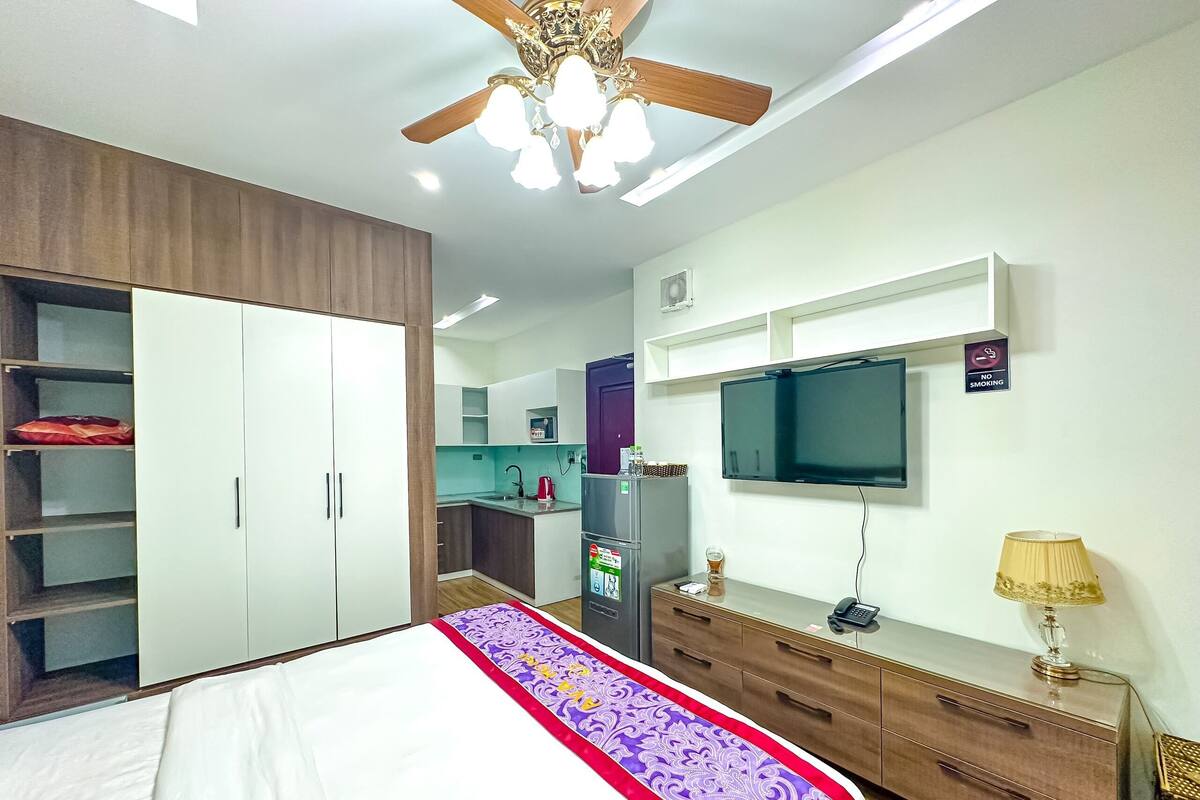 A bedroom with a bed, wardrobe, bedside table, lamp, and a TV mounted on the wall.