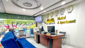Una reception di un hotel con un divano blu, una scrivania con computer e una parete orologio che mostra diversi fusi orari.