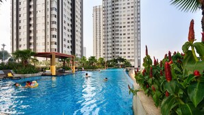 A swimming pool surrounded by high-rise buildings, with people swimming and a covered seating area.
