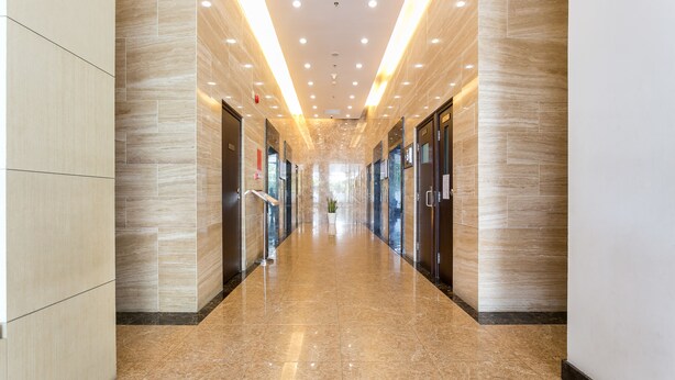 A modern hotel corridor with marble floors, recessed lighting, and glass doors on both sides.